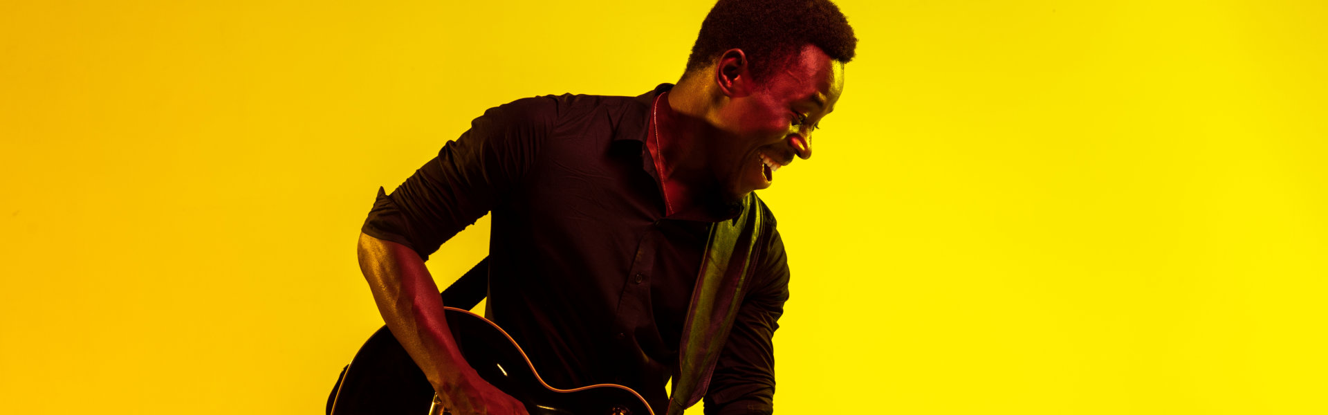 Young african-american musician playing the guitar like a rockstar on yellow background